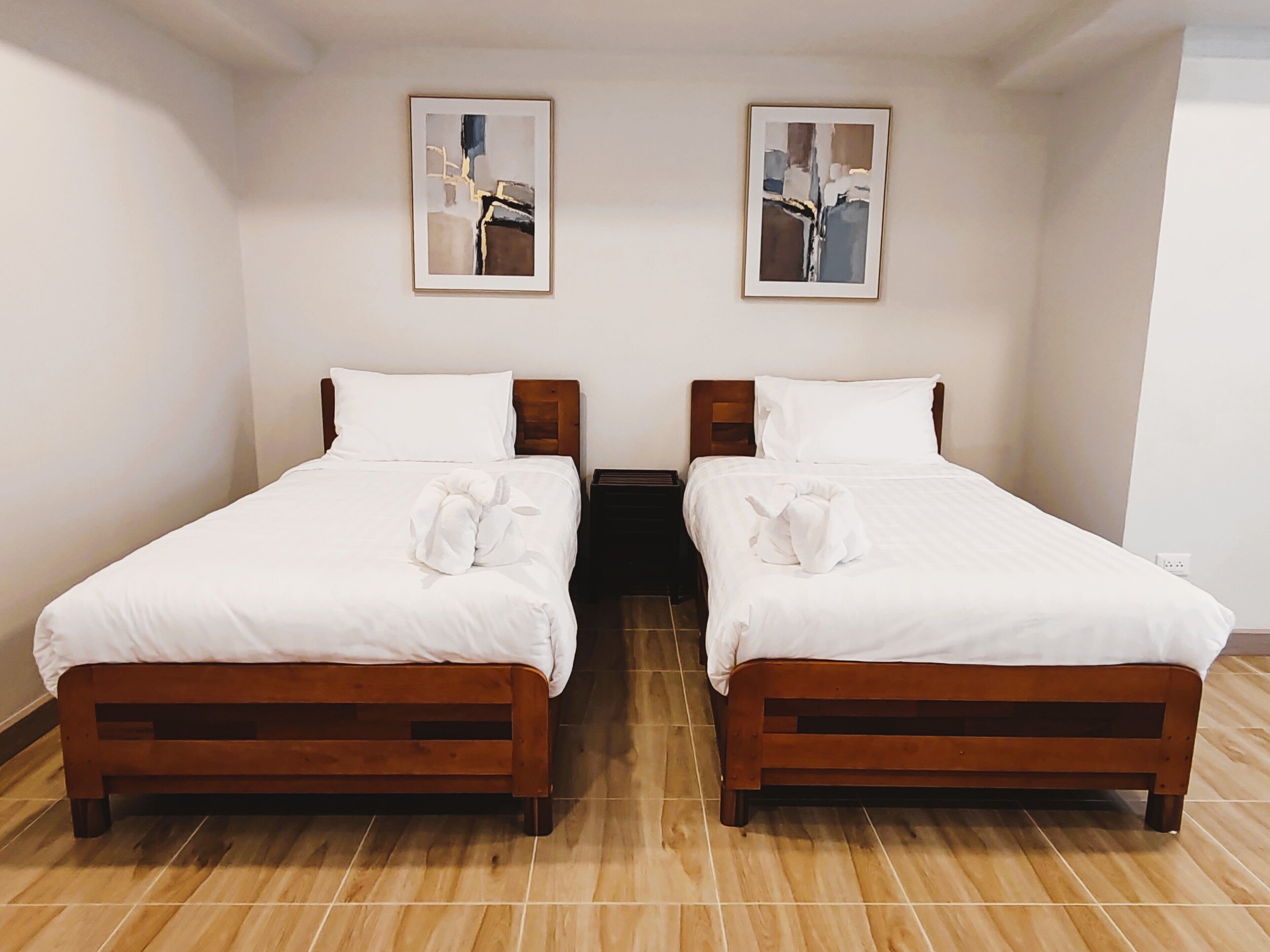 A room with two wooden beds, white bedding, and two abstract paintings on the walls.