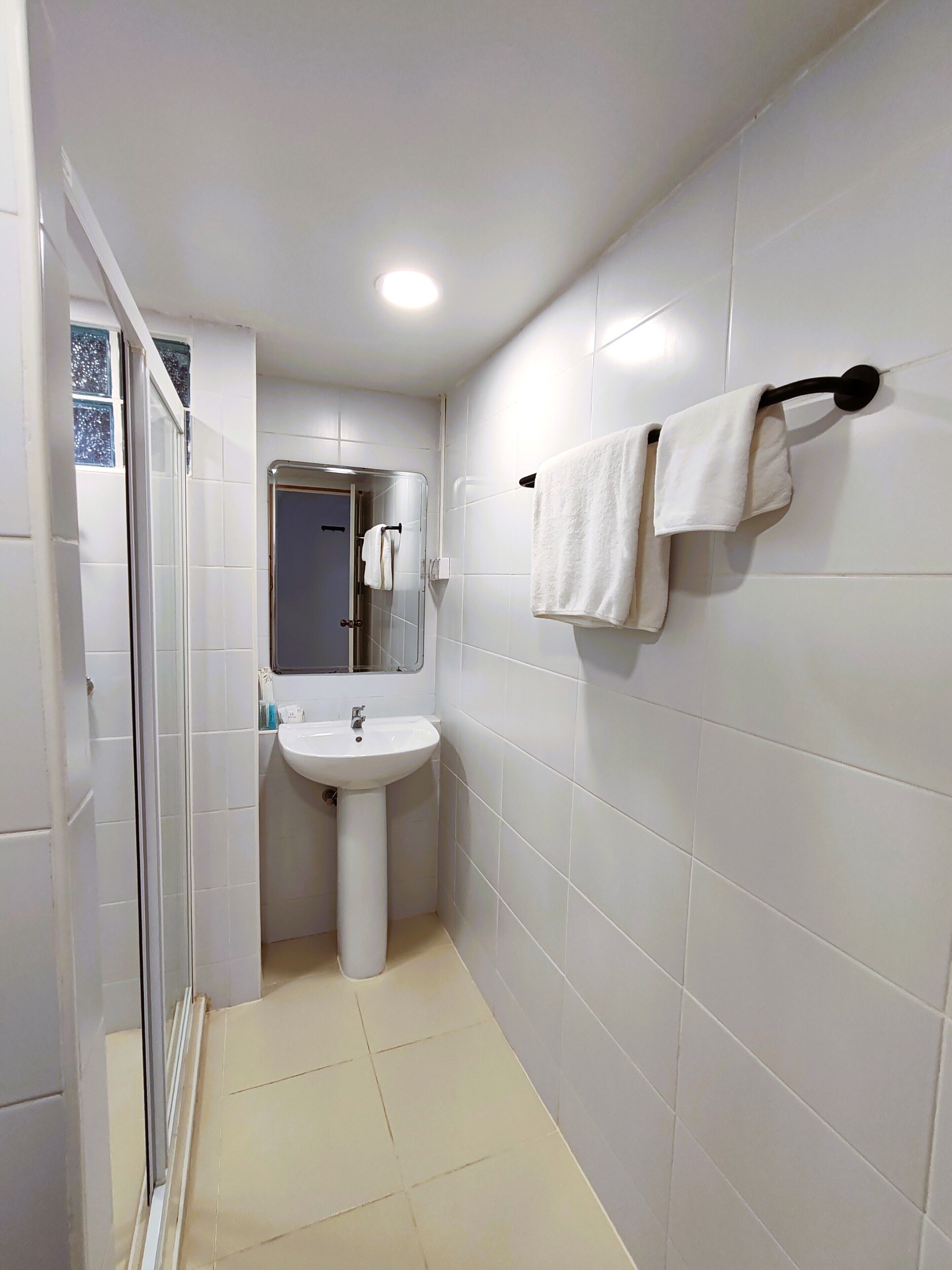 Un baño con cabina de ducha de vidrio, un lavabo sobre pedestal y un perchero con dos toallas.