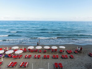 A beach with rows of red lounge chairs and white umbrellas, a sandy shore, and the ocean in the background.