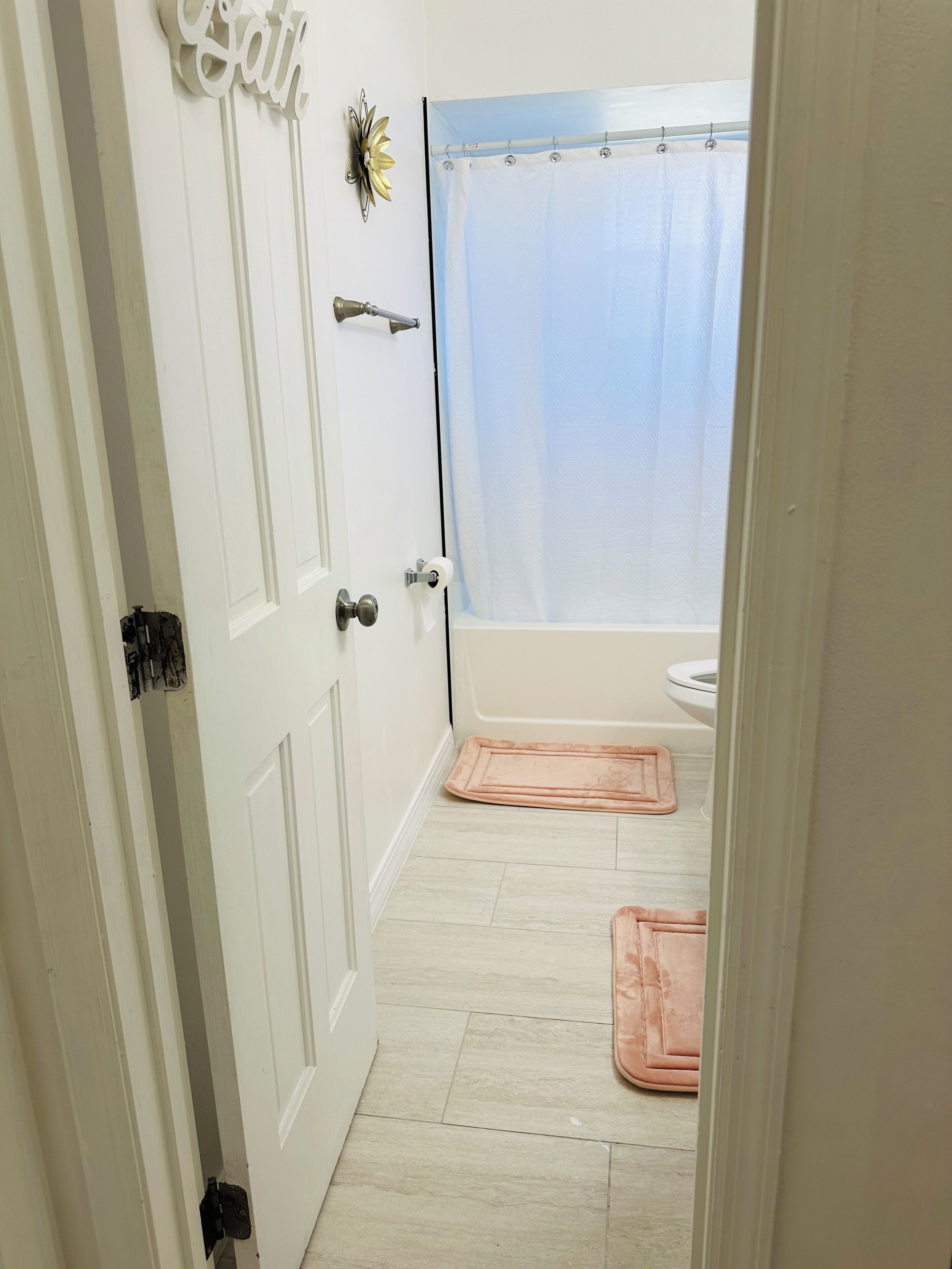 A bathroom with a shower curtain, a toilet, and a door with a nameplate.