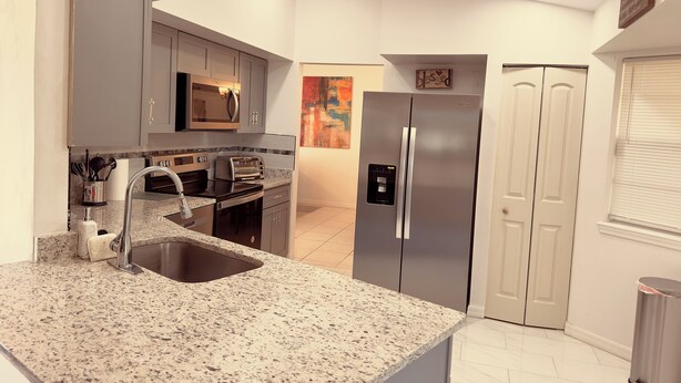 A modern kitchen with granite countertops, stainless steel appliances, and a two-door refrigerator. - Classy Comfy 3-bedroom house with AC in Palm Bay (Palm Bay)