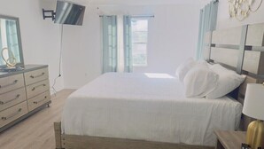 A bedroom with a bed, a TV mounted on the wall, a desk with a lamp, and a window with curtains. - Classy Comfy 3-bedroom house with AC in Palm Bay (Palm Bay)