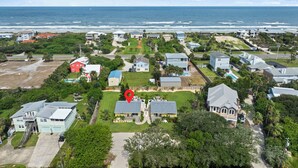 An aerial view of a coastal residential area with houses, a swimming pool, and a beach in the background.