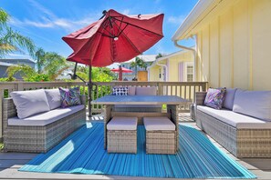 Un patio exterior con mobiliario de mimbre, una mesa y un paraguas rojo.