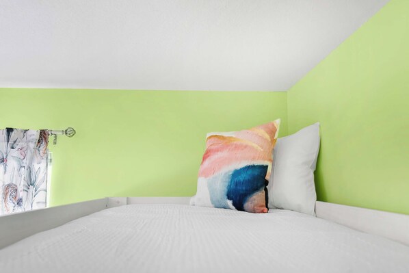 A bedroom with a bed, a colorful pillow, and a green wall.