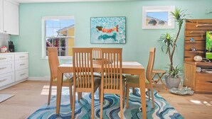 A dining area with a table and chairs, a painting on the wall, a window, and a plant.