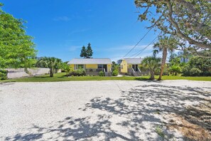 A two-story yellow building with a gravel driveway and a fenced yard.