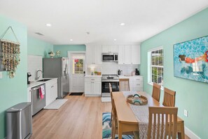 A modern kitchen with white cabinets, stainless steel appliances, and a dining area with a wooden table and chairs.