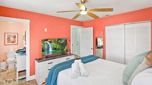 A bedroom with a bed, a television, a ceiling fan, a wardrobe, and a bathroom with a toilet and sink.