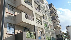 A multi-story residential building with balconies, a parking area, and a car parked in front.