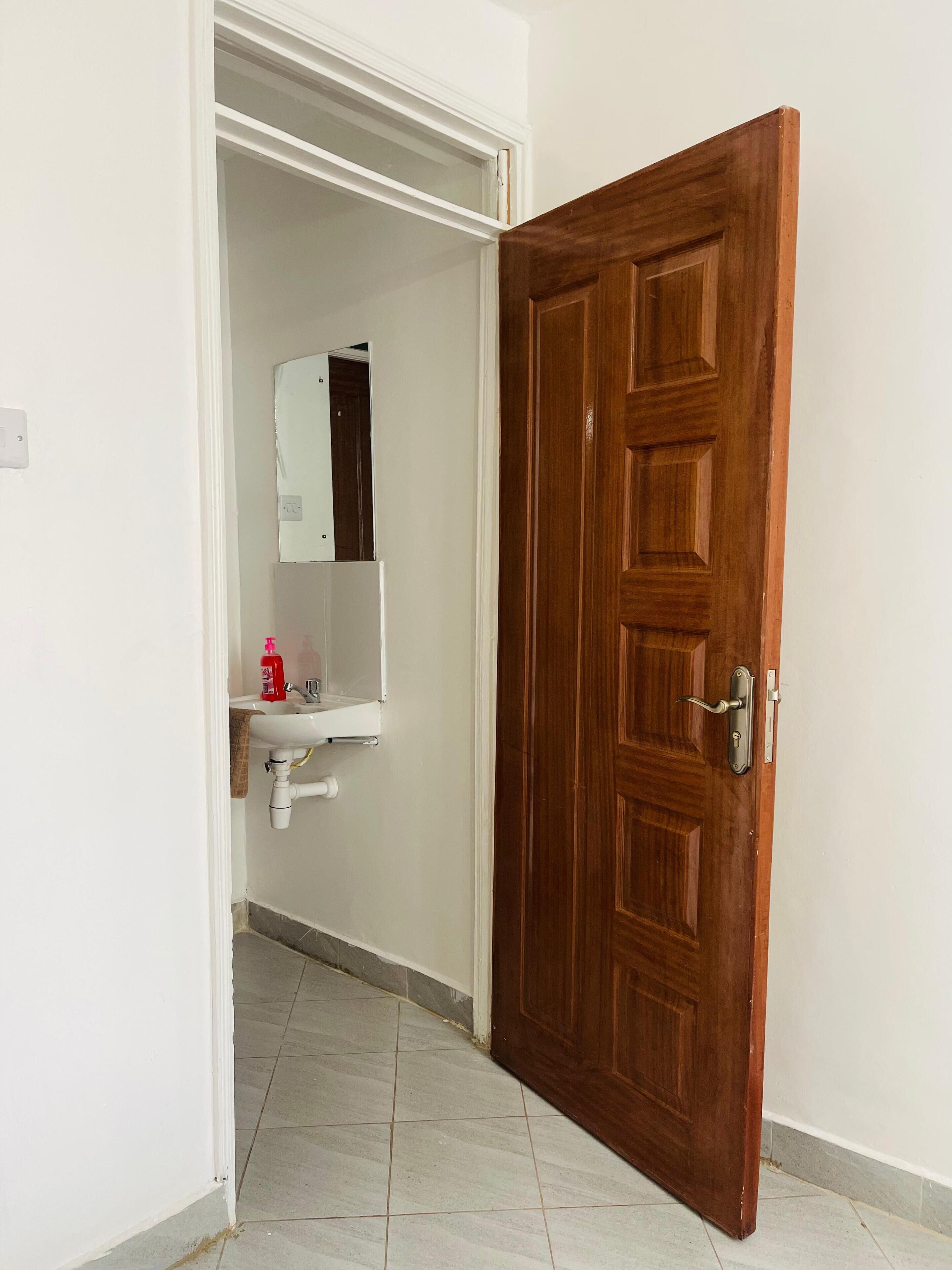 A bathroom with a wooden door, a white sink, and a mirror.