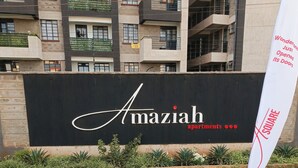 A sign for Amaziah apartments with a modern building in the background.