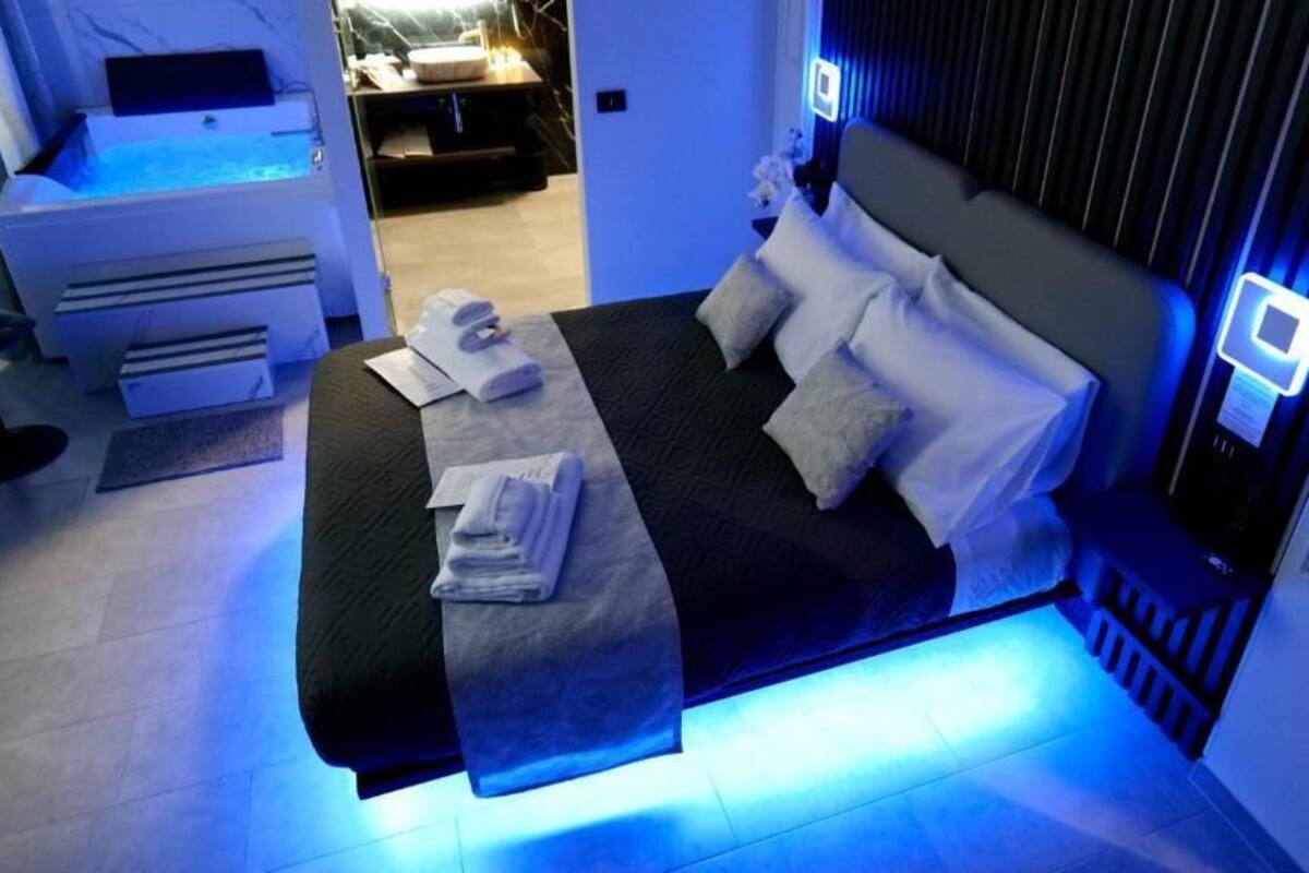 A modern hotel room with a bed, a small desk with a computer, and a massage chair.