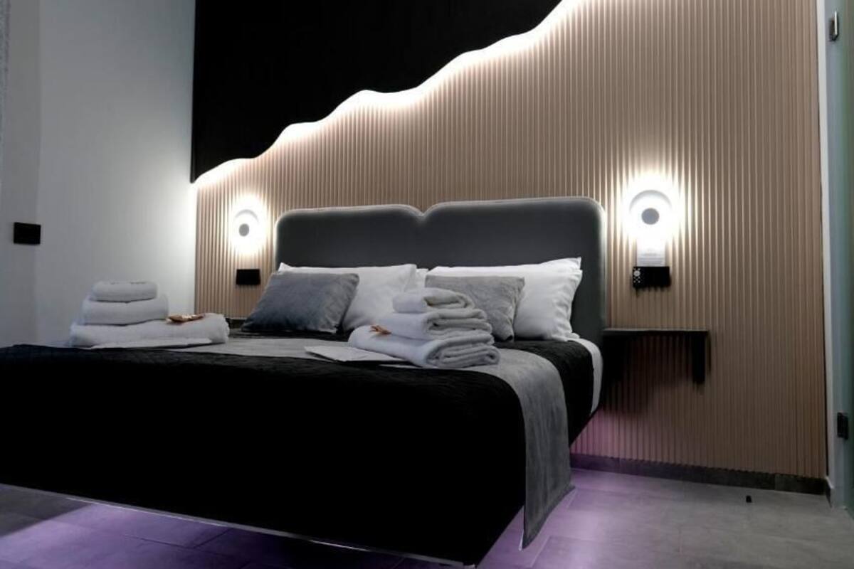 A modern bedroom with a large bed, two wall-mounted lights, and a wooden headboard.