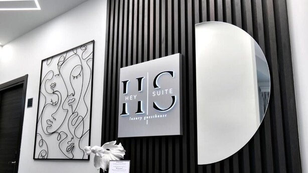 Un interior moderno con una obra de arte abstracta enmarcada, un letrero que dice 'Hey Suite Luxury Guesthouse' y un espejo curvo.