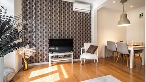 A modern living room with a patterned wallpaper, a flat-screen TV, a white sofa, and a dining area with chairs and a table. - Amomum Black Apartment, Anjos, Lisbon (Lisboa)