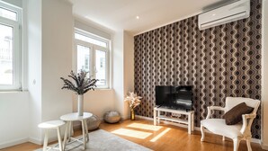 A modern living room with a patterned wallpaper, a flat-screen TV, a white sofa, and a small white table with two stools. - Amomum Black Apartment, Anjos, Lisbon (Lisboa)