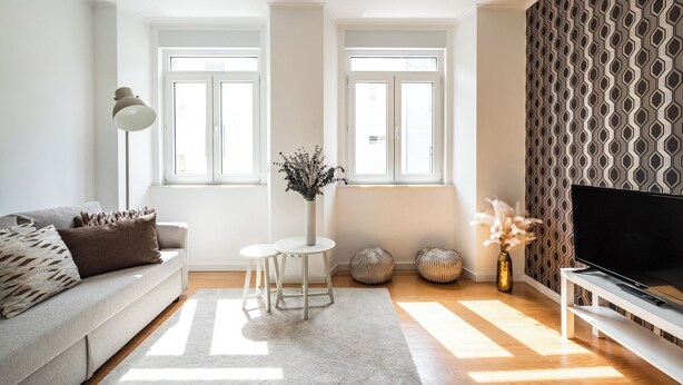A modern living room with a sofa, a small round table, a vase with flowers, a television on a stand, and patterned wallpaper. - Amomum Black Apartment, Anjos, Lisbon (Lisboa)