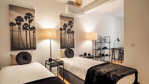 A modern hotel room with two beds, a desk, and a chair. There are wall-mounted lamps and a ceiling fan. - Amomum Black Apartment, Anjos, Lisbon (Lisboa)