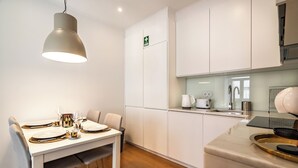 A modern kitchen with white cabinets, a dining table set with plates and cutlery, and a hanging pendant light. - Amomum Black Apartment, Anjos, Lisbon (Lisboa)