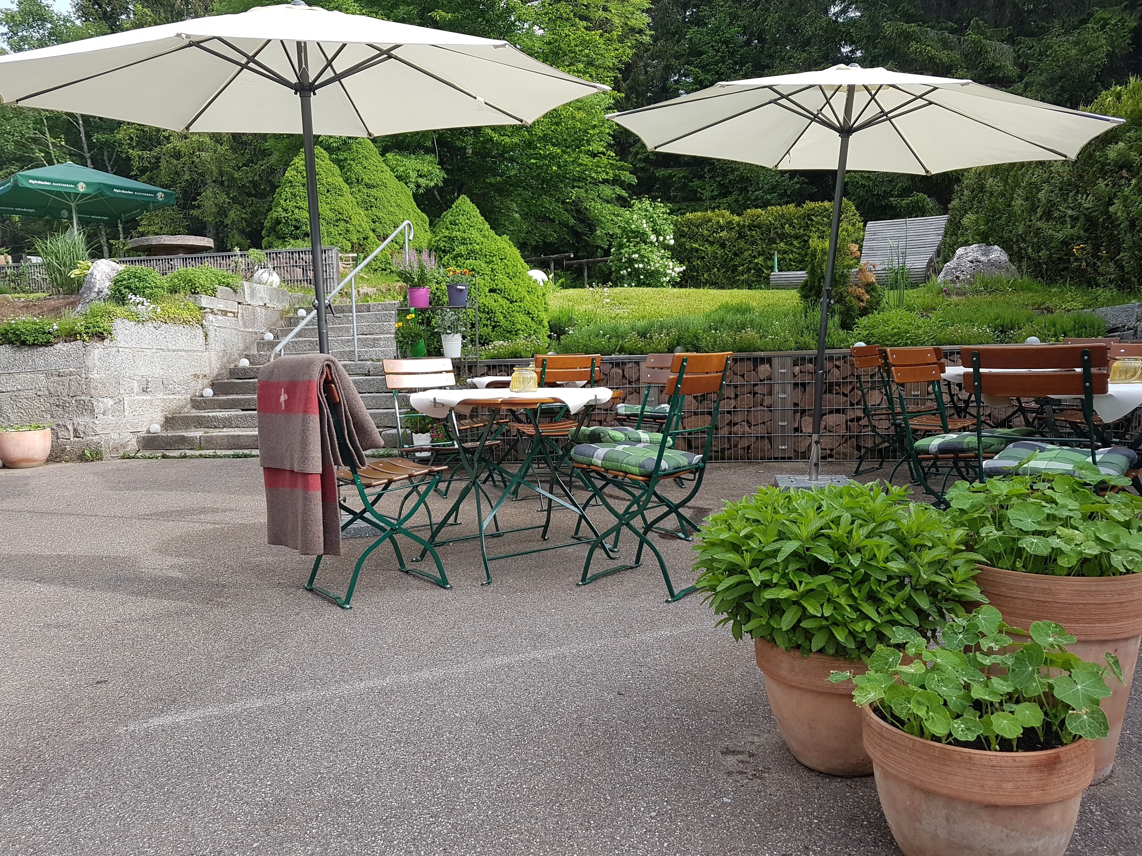 Un espace extérieur aménagé en terrasse, avec des tables et des chaises, de grands parasols et des plantes en pot.