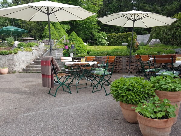 Un patio al aire libre con mesas y sillas, sombrillas grandes y plantas en macetas.