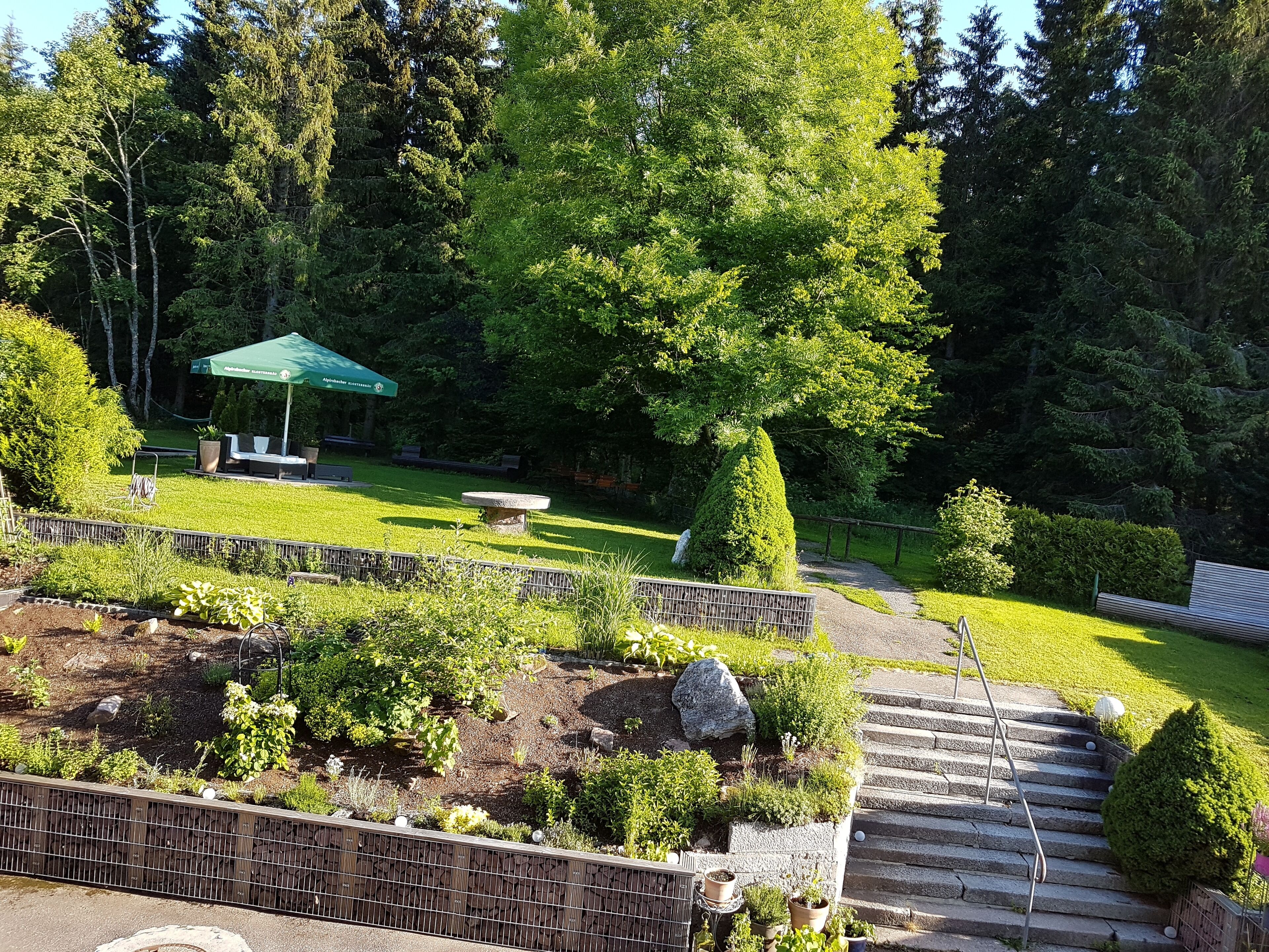 A garden with a stone bench, a green umbrella, and a stone staircase leading up.