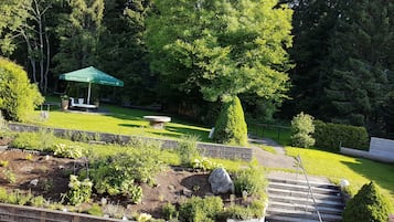 Ein Garten mit einer Steinsitzbank, einem grünen Sonnenschirm und einer Steintreppe, die nach oben führt.
