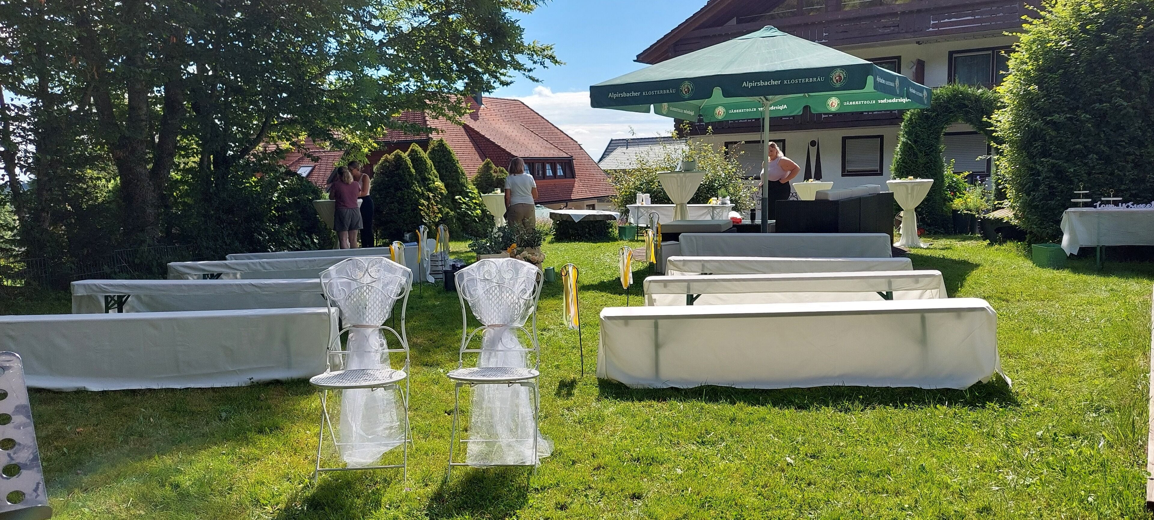 An outdoor event setup with tables and chairs, a green umbrella, and a building in the background.