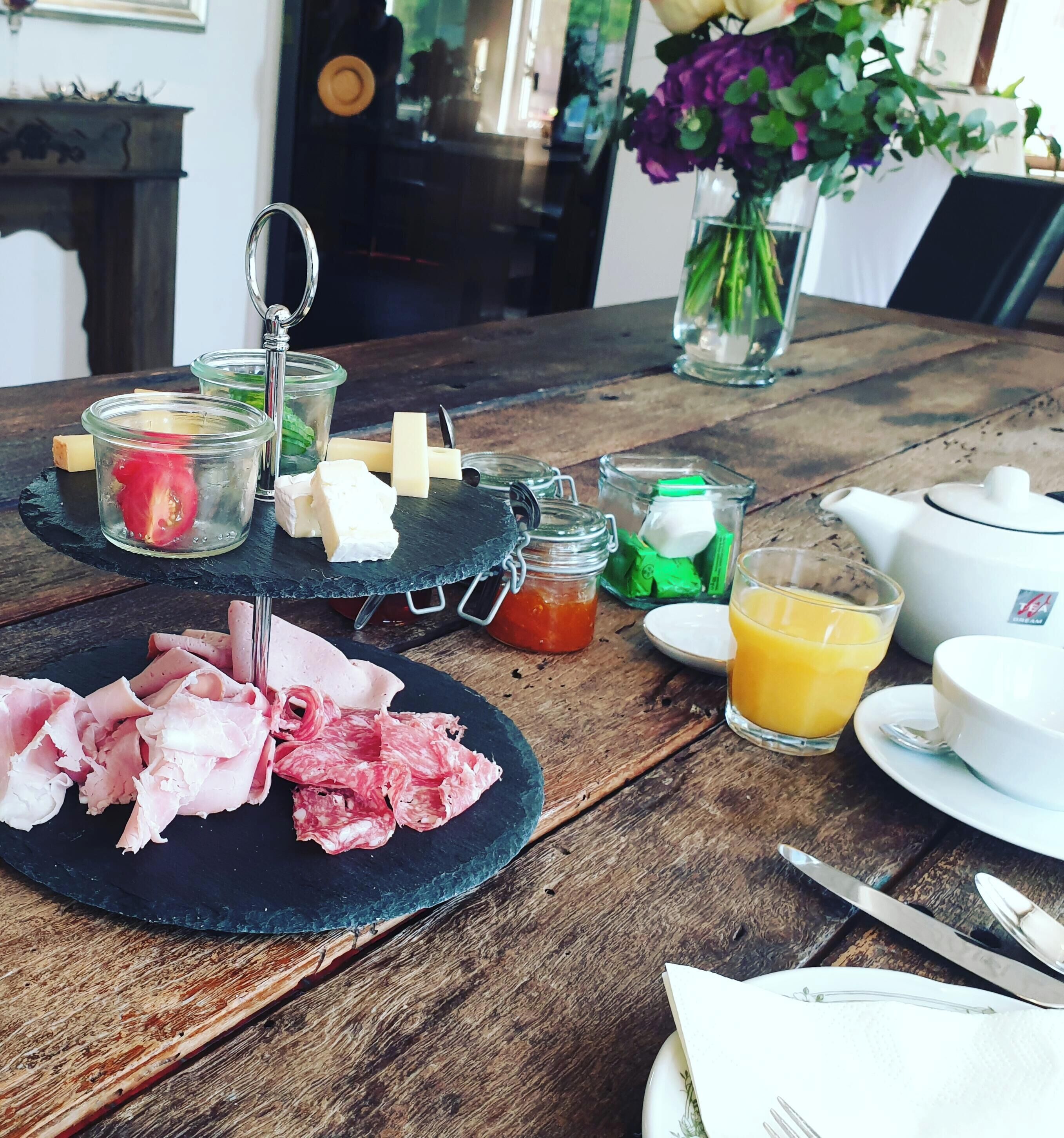 Une table en bois sur laquelle repose un plateau noir en ardoise, servant de présentoir pour divers aliments, ainsi qu'un verre de jus d'orange et une théière.