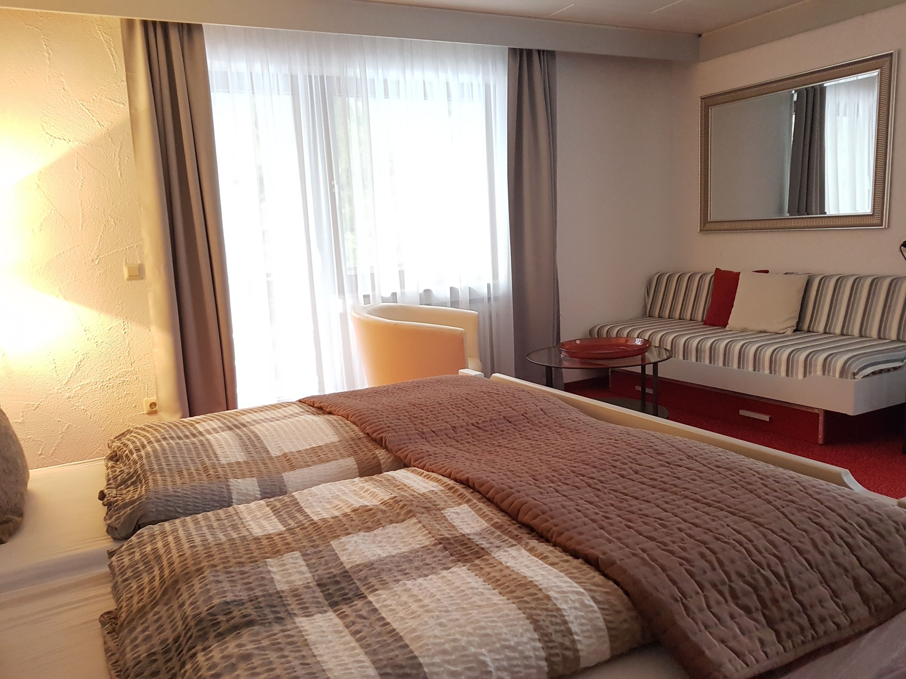 A hotel room with a bed, a chair, a sofa, and a large mirror.