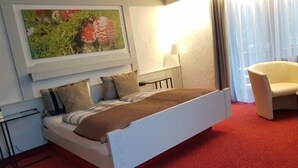 Habitación de hotel con cama, almohadas, lámpara, silla y un cuadro en la pared.