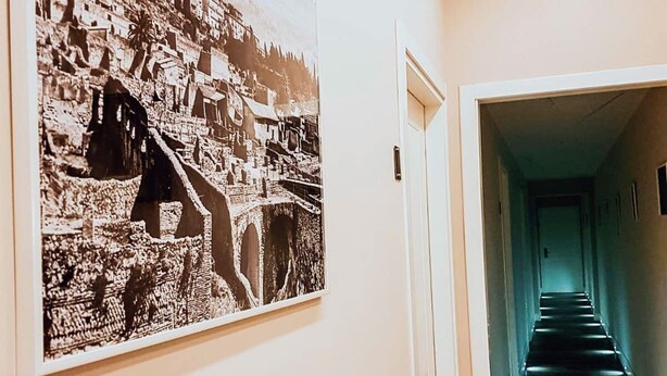 Un pasillo con una fotografía en blanco y negro de un pueblo montañoso y una escalera que conduce a otra habitación.