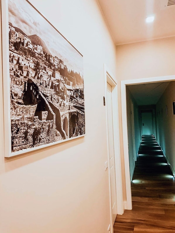 Un pasillo con una fotografía en blanco y negro de un pueblo montañoso y una escalera que conduce a otra habitación.