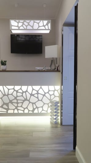 Un área de recepción moderna con un separador de diseño de piedra, un televisor de pantalla plana y una lámpara minimalista.