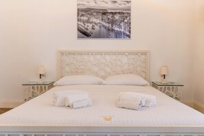 Habitación de hotel con una cama grande, dos mesitas de noche, un cuadro colgado en la pared y toallas dobladas con esmero.