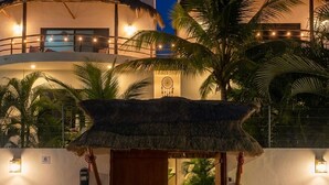 Een resort met een rieten entree, potplanten en een goed verlicht gebouw op de achtergrond.