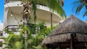 Een resort terras met een rieten parasol, witte stoelen en een eettafel.
