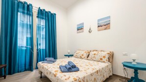 Un dormitori amb un llit, una taula de nit, una taula i una finestra amb cortines.