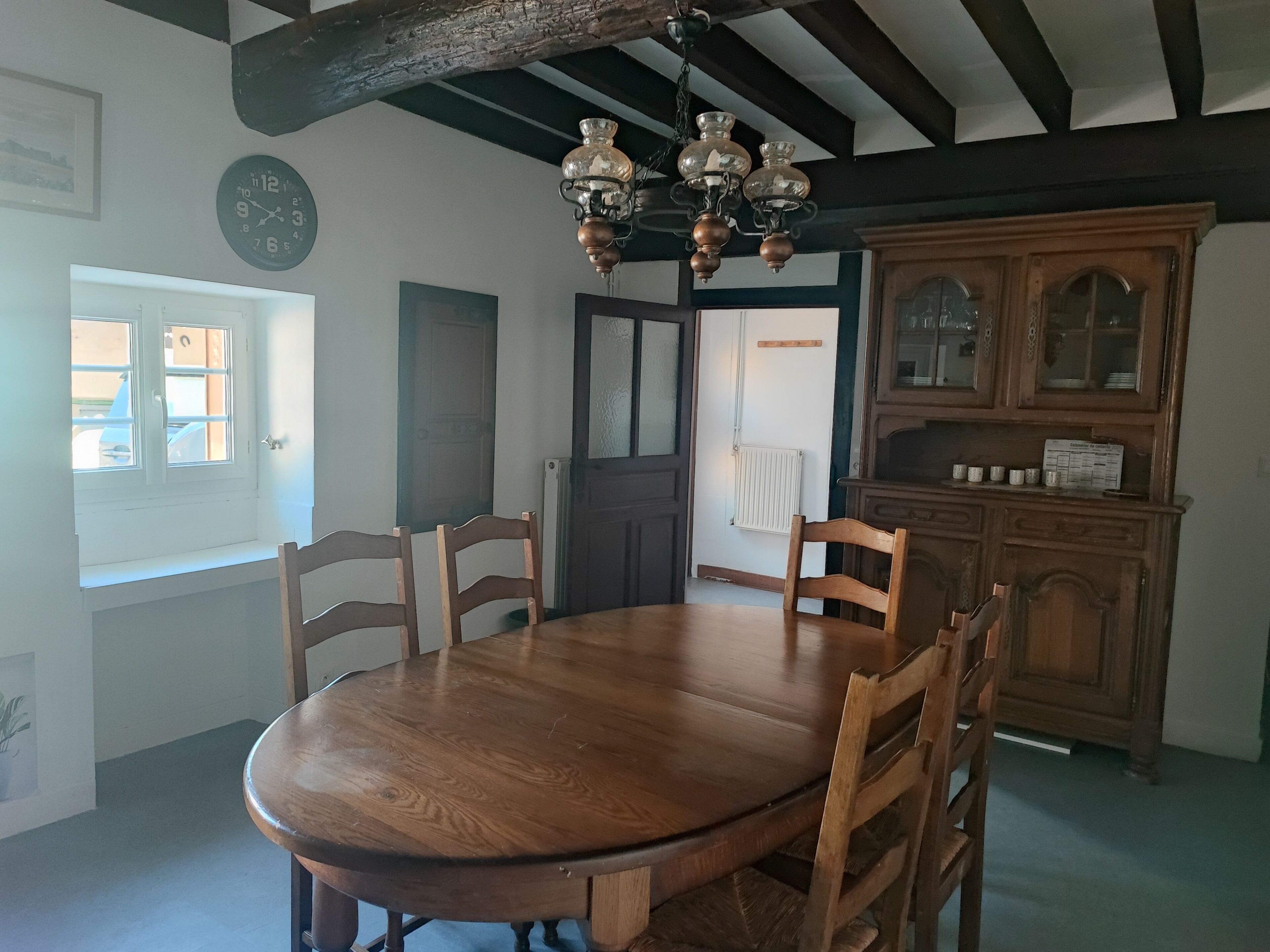 A dining room with a wooden table and chairs, a chandelier, and a wooden cabinet.
