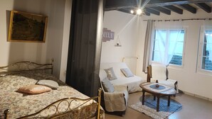 A bedroom with a bed, a chair, a small table, a radiator, and a window with curtains.