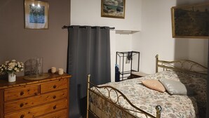 A bedroom with a wooden dresser, a bed with floral bedding, a metal bed frame, a black metal shelf, and two framed pictures on the wall.