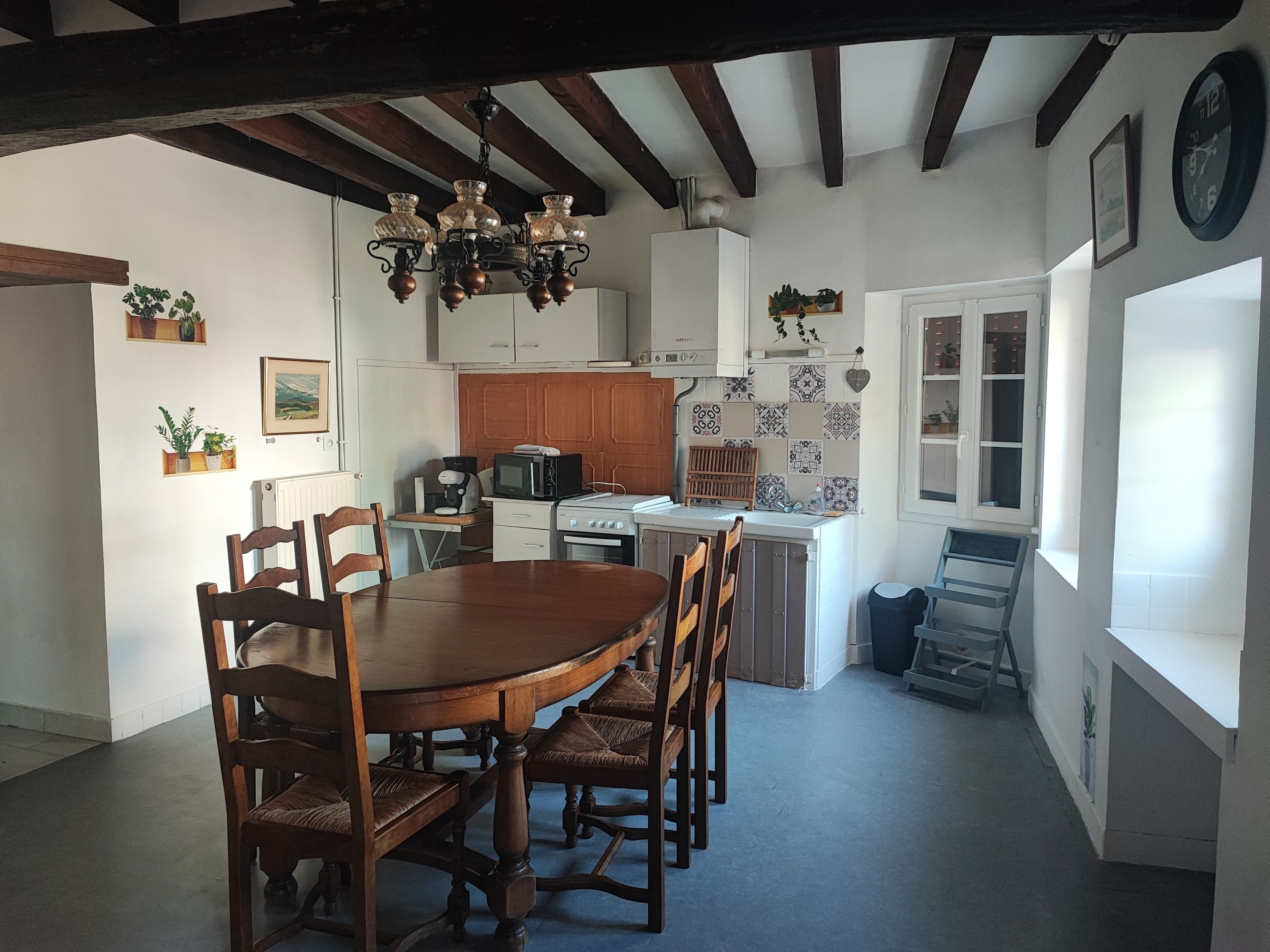 A dining area with a wooden table and chairs, a kitchen with white cabinets, and a chandelier.