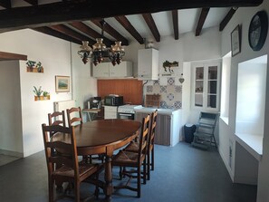 Un coin repas avec une table et des chaises en bois, une cuisine avec des meubles blancs et un lustre.