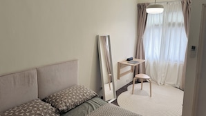 Ein gemütlicher, kompakter Raum mit einer Couch, einem kleinen Tisch mit einem Laptop, einer Stehlampe und einem runden Teppich.
