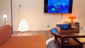 Ein modernes Wohnzimmer mit einem an der Wand montierten Flachbildfernseher, einem runden Couchtisch, einer Couch, einer Stehlampe und einer dekorativen Papierlaterne.