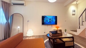 Ein modernes Wohnzimmer mit einer Couch, einem an der Wand befestigten Flachbildfernseher, einer Lampe und einer Treppe.