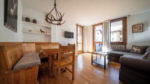 A cozy living room with wooden furniture, a television, and a large window offering a view of buildings outside.
