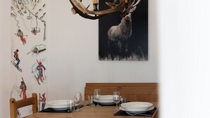 A dining area with a wooden table set for four, a mounted deer head on the wall, and a mural of skiers on the wall.