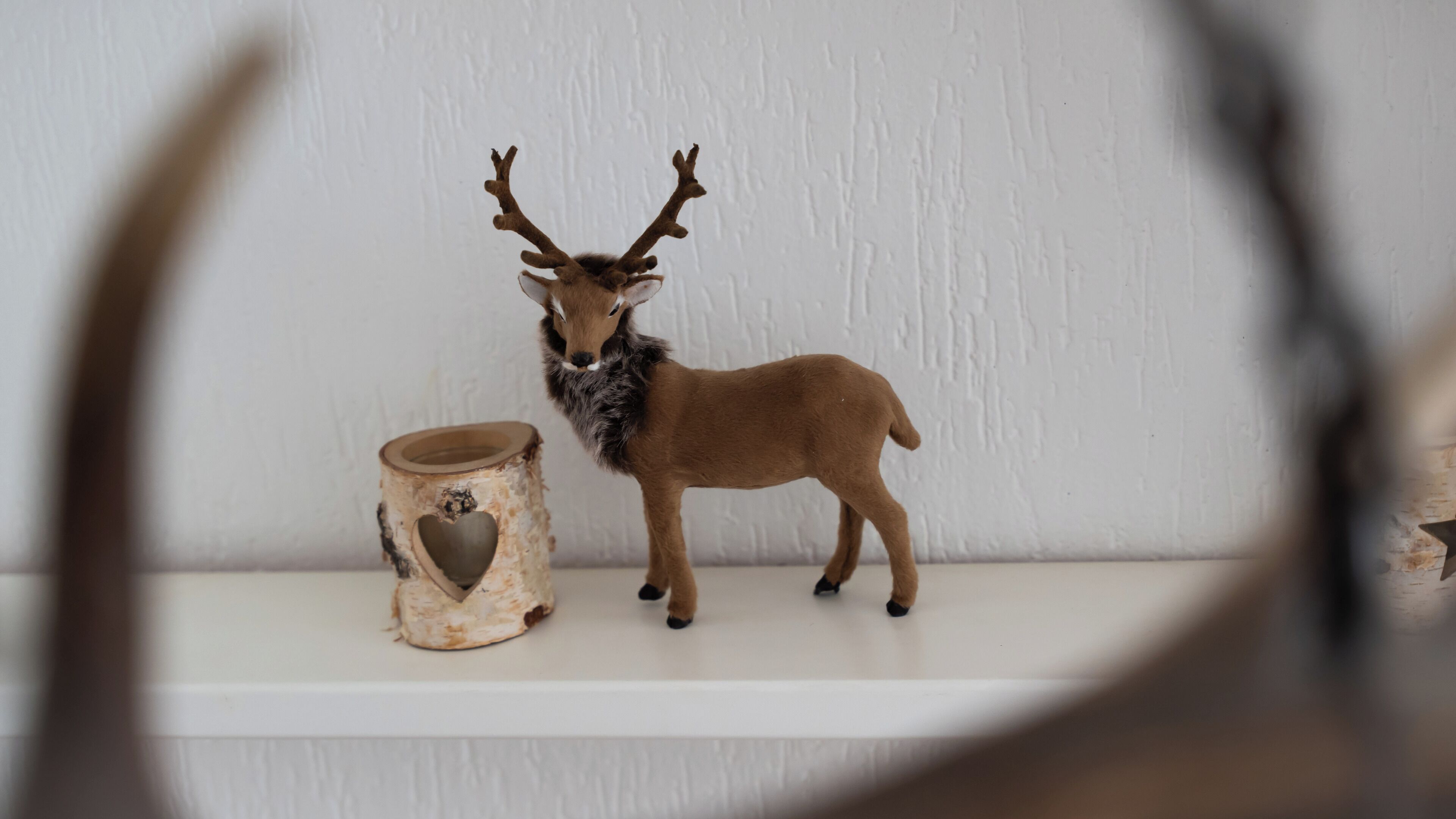 A small deer figurine on a shelf next to a rustic wooden container with a heart cutout.